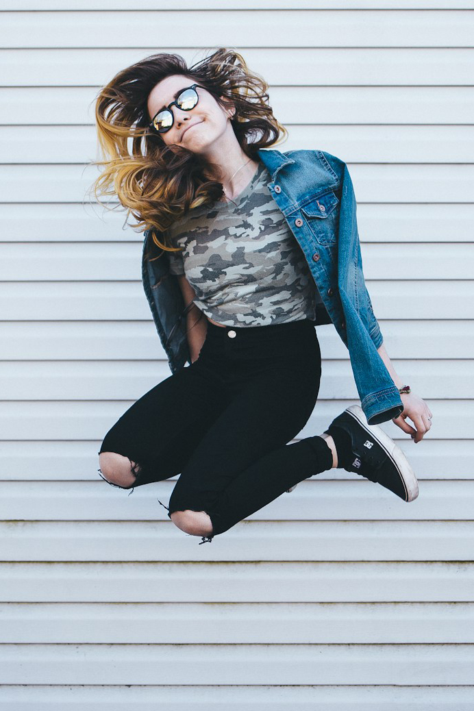 woman in torn jeans dances in front of white-sided wall