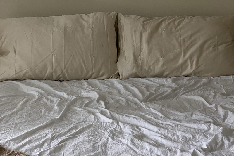 pale neutral bed with two pillows and rumpled sheet