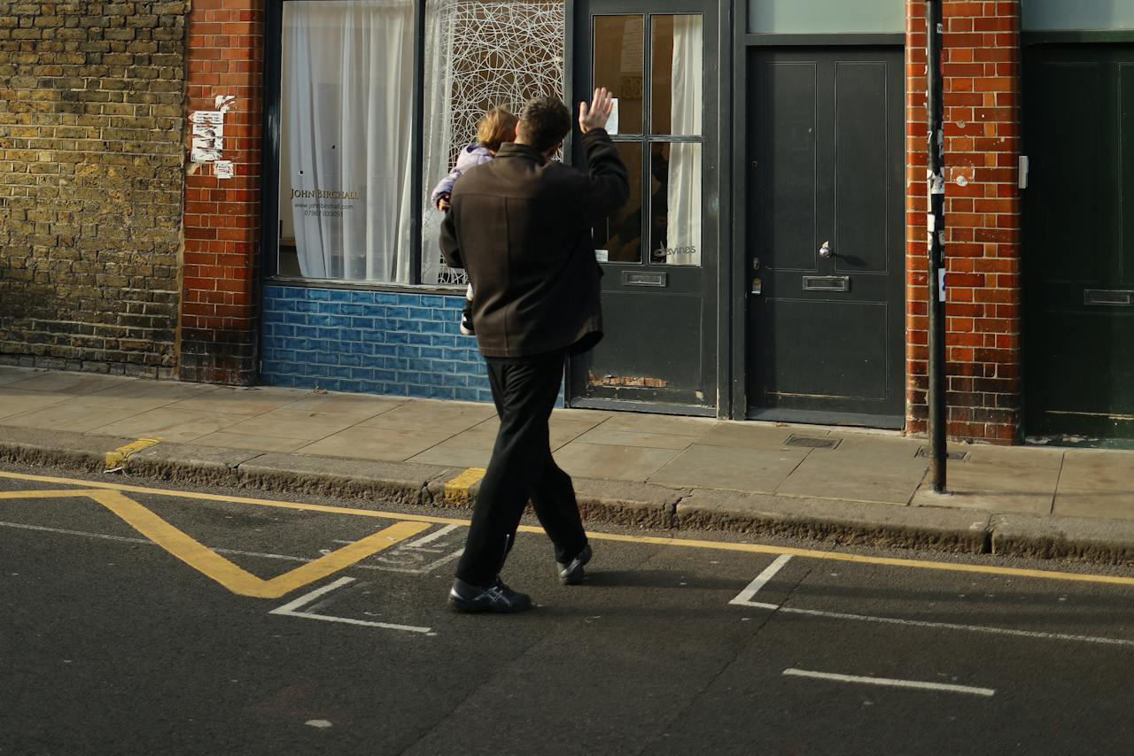 man carrying yound child jaywalking on quiet street