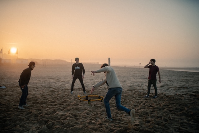 four people play roundnet on beach at sunset