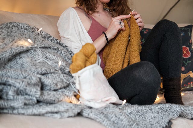 cropped view of woman seated on sofa, knitting