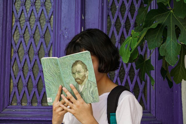 woman's face obscured by book with Van Gogh self-portrait on cover, outdooers